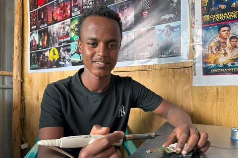 Abraham aus Debre Berhan erhielt von Menschen für Menschen Startkapital für seinen Mobiltelefon-Reparaturladen Abraham repariert ein defektes Mobilgerät mit einem Lötkolben.