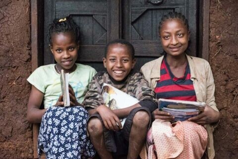 Drei Kinder mit Schulbüchern vor einer Haustüre