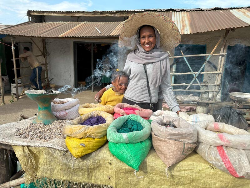 Marktverkäuferin steht mit Kind vor farbigen Säcken gefüllt mit Weihrauch