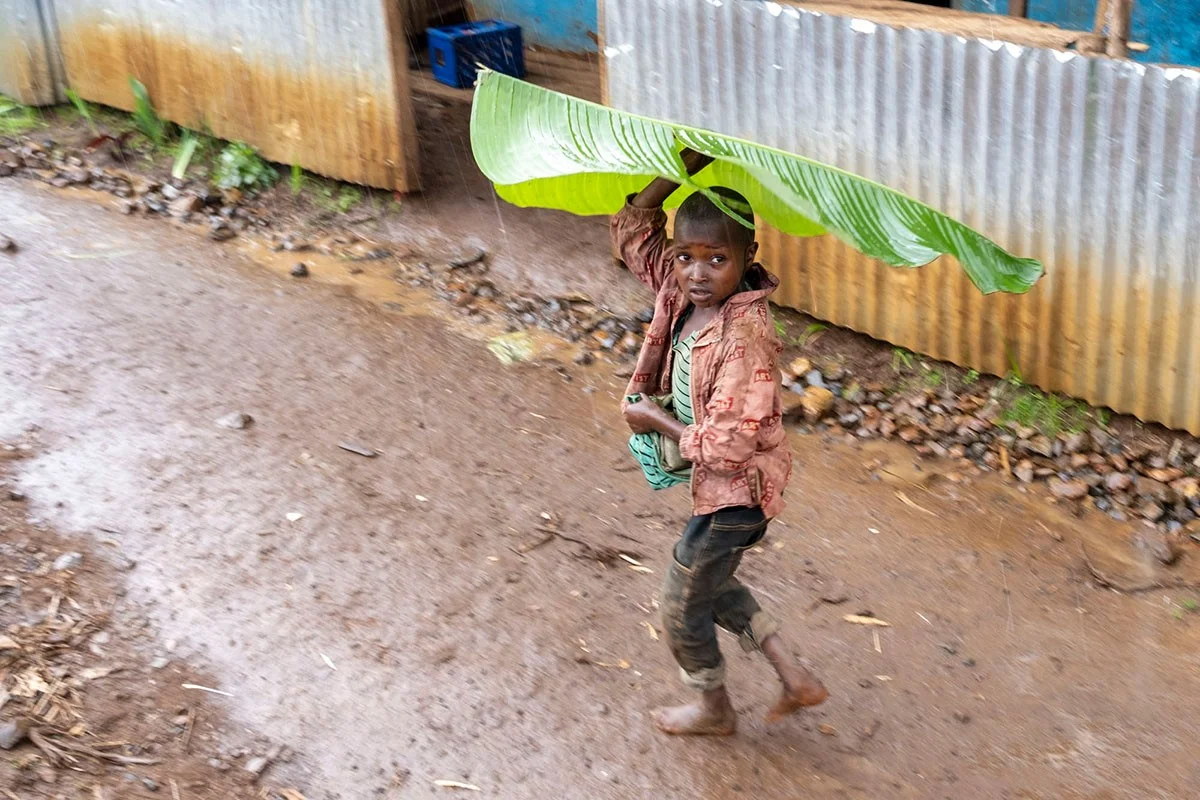 Kind mit Enseteblatt auf dem Kopf | Stiftung Menschen für Menschen Ein Junge schützt sich mit einem Enseteblatt vor dem Regen