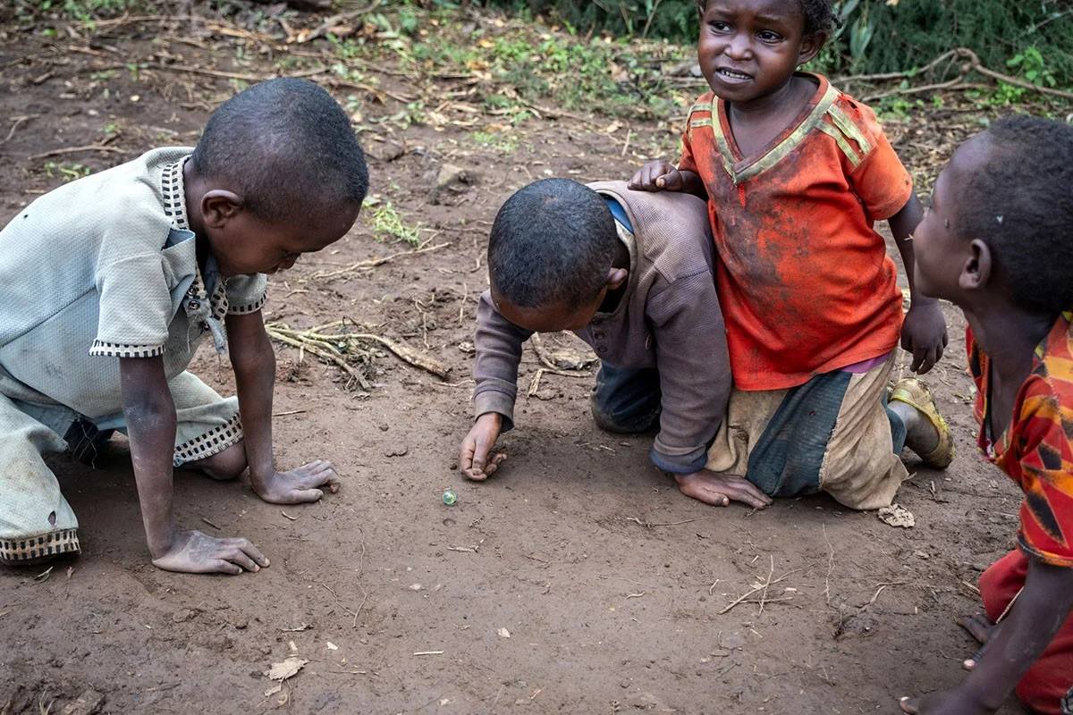 Arme Kinder spielen am Boden mit Murmeln