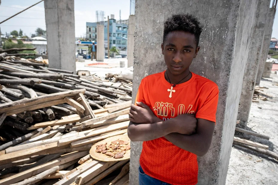 Junge steht mit verschränkten Armen bei einer Baustelle