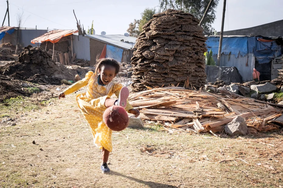 Junges Mädchen spielt in einem gelben Kleid Fussball
