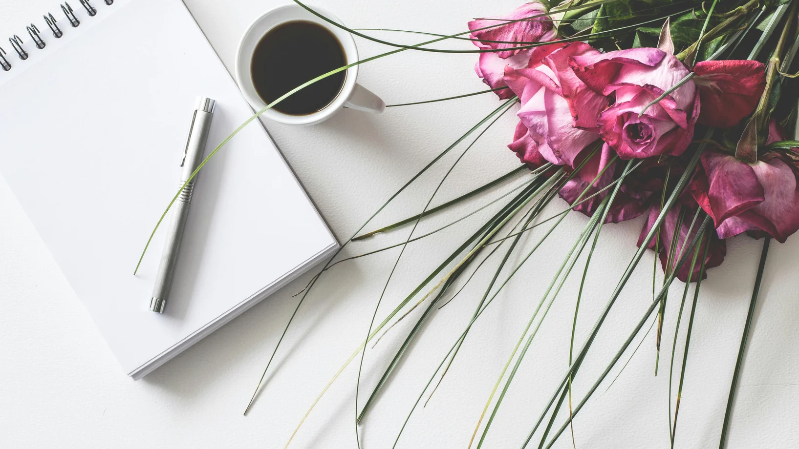 Red rose flowers bouquet on white surface beside spring book with click pen and cup of cofffee